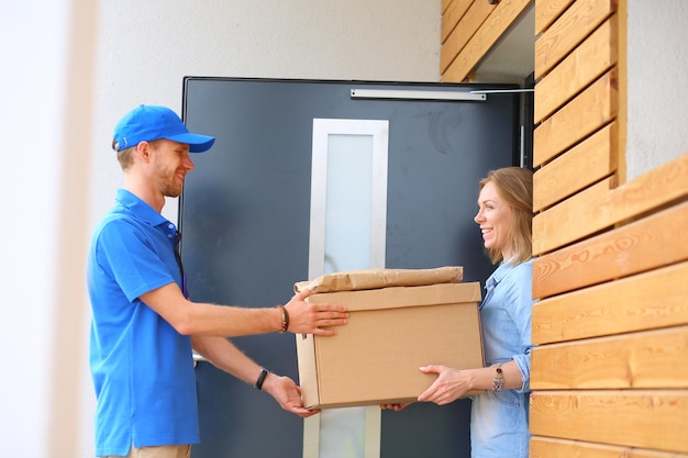 Lächelnder Lieferbote in blauer Uniform, der Paketbox an das Kurierdienstkonzept des Empfängers liefert Lächelnder Lieferbote in blauer Uniform