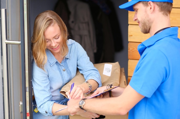Lächelnder Lieferbote in blauer Uniform, der Paketbox an das Kurierdienstkonzept des Empfängers liefert Lächelnder Lieferbote in blauer Uniform