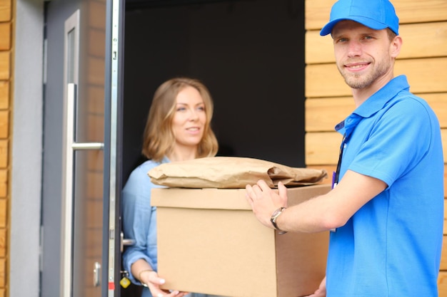 Lächelnder Lieferbote in blauer Uniform, der Paketbox an das Kurierdienstkonzept des Empfängers liefert Lächelnder Lieferbote in blauer Uniform