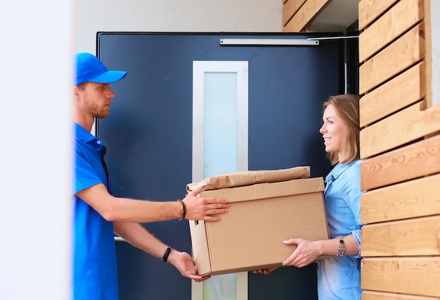 Lächelnder Lieferbote in blauer Uniform, der Paketbox an das Kurierdienstkonzept des Empfängers liefert Lächelnder Lieferbote in blauer Uniform