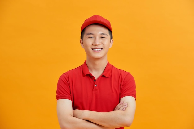 Lächelnder Lieferbote in roter Uniform stehend mit verschränktem Arm - isoliert auf weißem Hintergrund