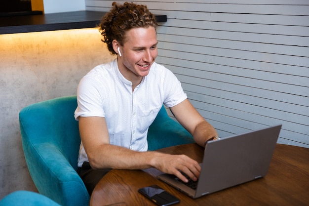Lächelnder lockiger Geschäftsmann mit Laptop-Computer beim Sitzen am Tisch im Café