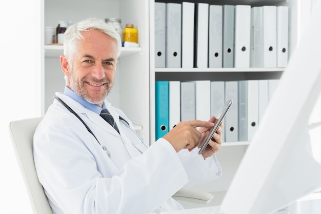 Lächelnder männlicher Doktor, der digitale Tablette im Ärztlichen Dienst verwendet
