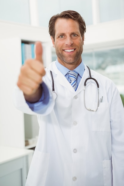 Lächelnder männlicher Doktor, der oben Daumen im Ärztlichen Dienst gestikuliert
