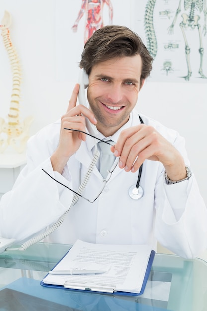 Lächelnder männlicher Doktor, der Telefon im Büro verwendet