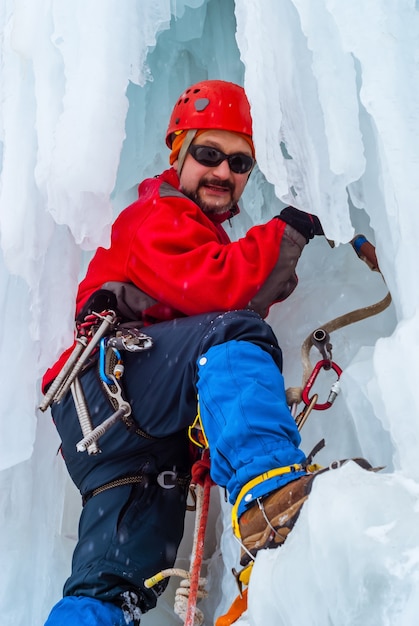 Lächelnder männlicher Kletterer mit Eispickel unter Eiszapfen eines gefrorenen Wasserfalls