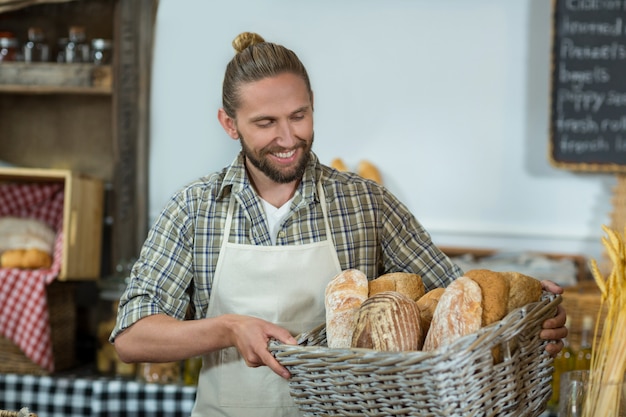 Lächelnder männlicher Stab, der einen Korb von Baguettes an der Theke hält