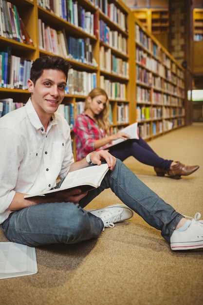 Lächelnder männlicher Student, der auf Boden in der Bibliothek überarbeitet