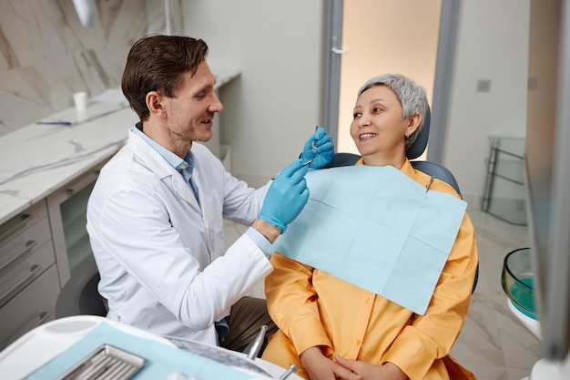 Lächelnder männlicher Zahnarzt, der mit einer älteren Frau im Büro einer Zahnklinik arbeitet