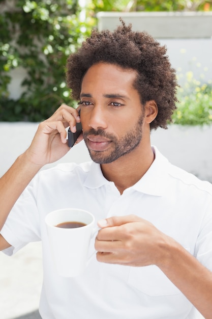 Lächelnder Mann am Telefon, das Kaffee trinkt