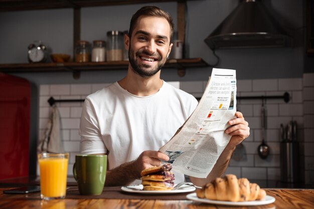 Lächelnder Mann beim Frühstück, Zeitung lesen