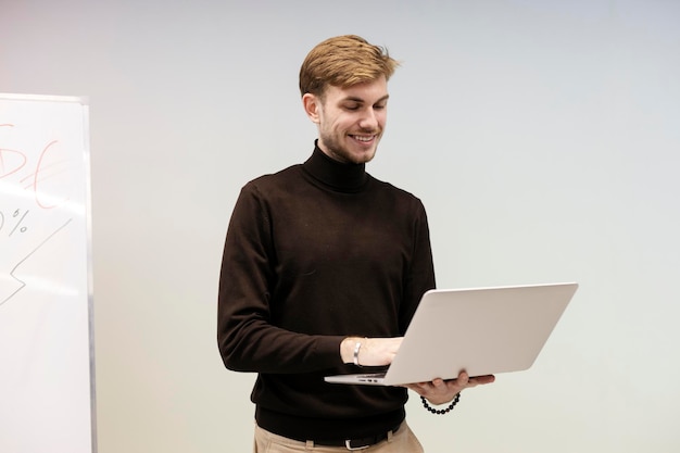 Lächelnder Mann, der am Laptop arbeitet, während er im modernen Büro steht Arbeit im Büro erfolgreicher Geschäftsmann