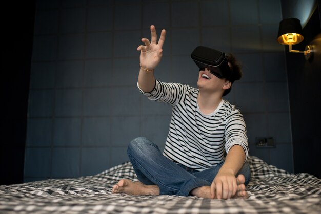 Lächelnder Mann, der auf Bett mit VR-Brille sitzt