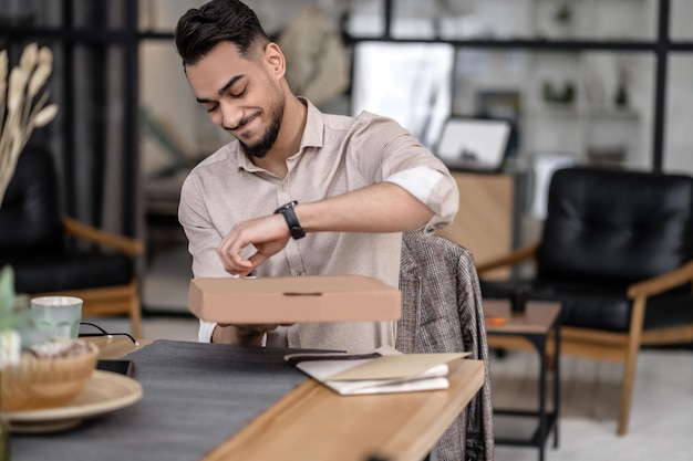 Lächelnder Mann, der die Box öffnet, die am Tisch sitzt