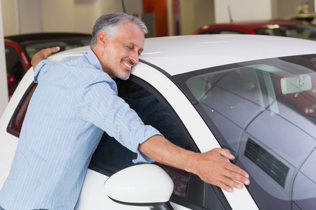 Lächelnder Mann, der ein weißes Auto umarmt