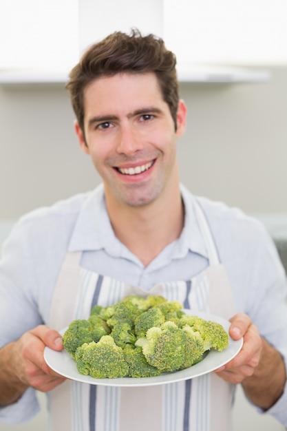 Lächelnder Mann, der eine Platte des Brokkolis in der Küche hält