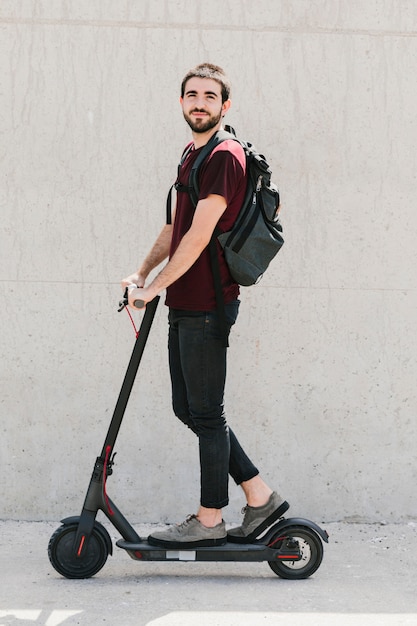 Lächelnder Mann, der einen E-Roller auf Straße reitet