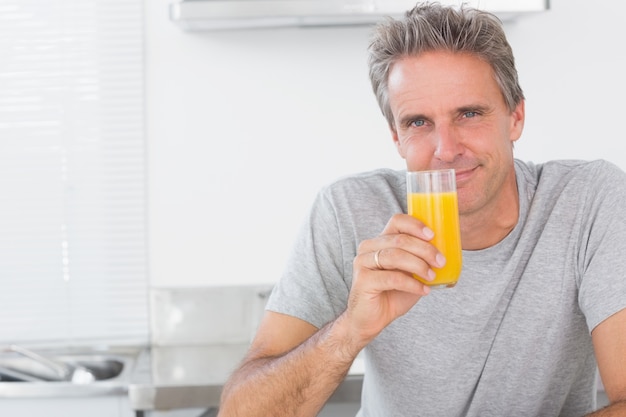 Lächelnder Mann, der Glas Orangensaft in der Küche isst