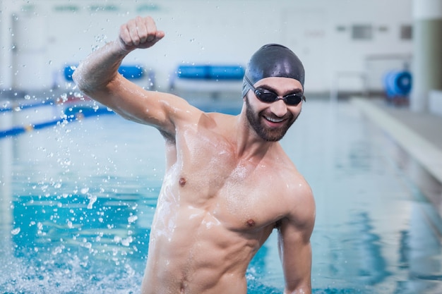 Lächelnder Mann, der mit dem angehobenen Arm am Pool triumphiert