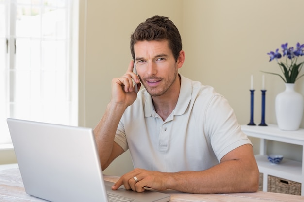 Lächelnder Mann, der zu Hause Laptop und Handy verwendet