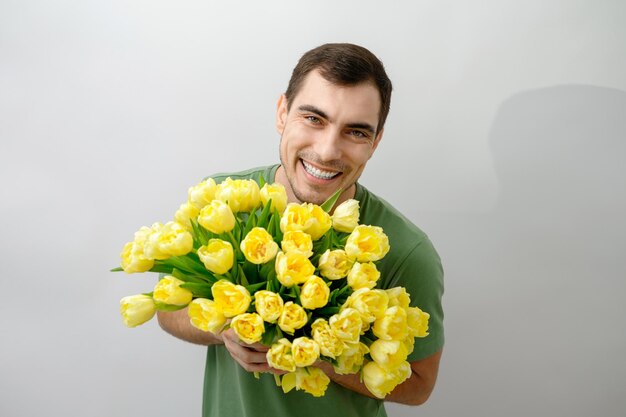 Lächelnder Mann im grünen T-Shirt mit Blumenstrauß gelbe Tulpen auf weißem Hintergrund kopieren Raum