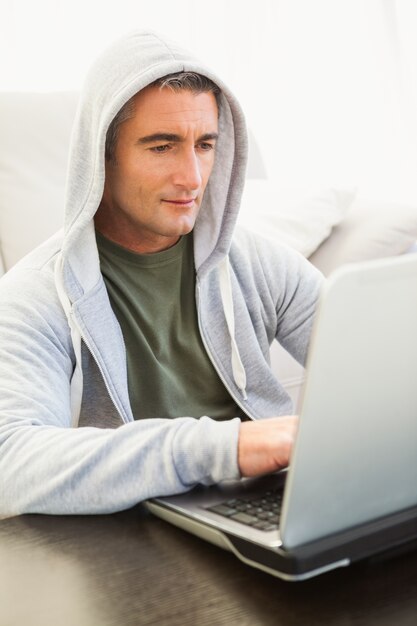 Lächelnder Mann in der Haubenjacke unter Verwendung des Laptops