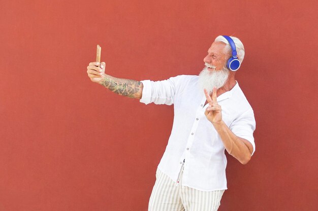 Lächelnder Mann macht ein Selfie und hört Musik, während er an der Wand steht