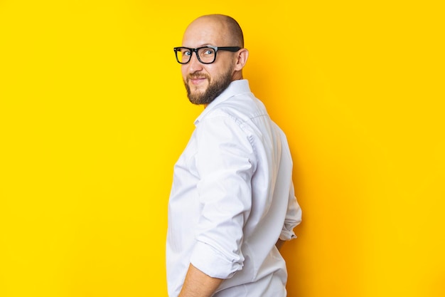 Lächelnder Mann mit Bart und Brille in einem weißen Hemd auf gelbem Hintergrund