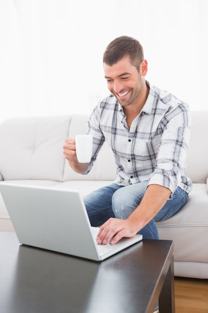 Lächelnder Mann mit einem Becher unter Verwendung eines Laptops