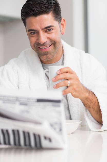 Lächelnder Mann mit Kaffeetasse-Lesezeitung in der Küche