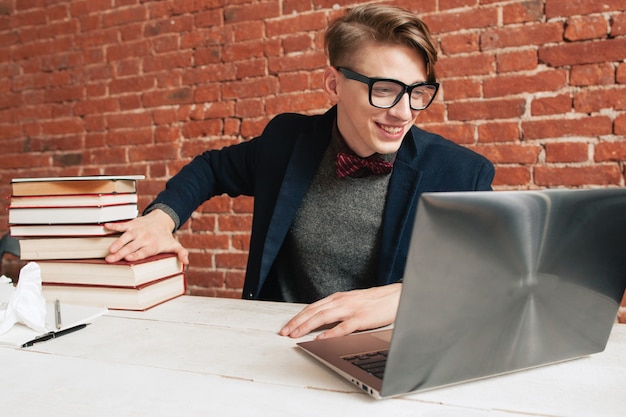 Lächelnder Mann mit Laptop entfernen Stapel Bücher.