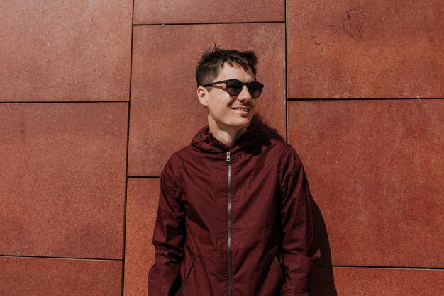 Lächelnder Mann mit Sonnenbrille, während er an der Wand steht