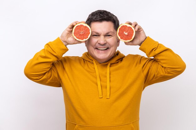 Lächelnder Mann mittleren Alters, der Spaß daran hat, zwei Hälften von Grapefruit zu halten, die positive Emotionen ausdrücken