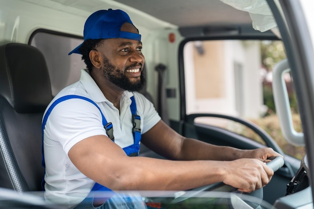 Lächelnder Mann-Mover-Arbeiter in blauer Uniform, der Lastwagen zum Liefer- und Umzugsservice fährt