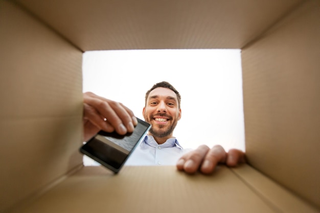 lächelnder Mann nimmt sein Smartphone aus der Paketbox