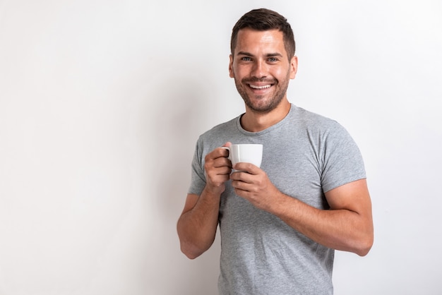 Lächelnder Mann steht mit Tasse Morgentee oder -kaffee und betrachtet die Kamera.