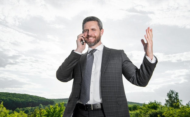 Lächelnder Mann telefoniert im Freien Mann telefoniert im Anzug Foto eines Mannes telefoniert Mann telefoniert vor Himmelshintergrund