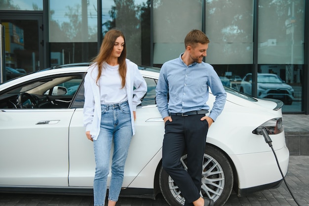 Lächelnder Mann und Frau an der Ladestation für Elektroautos Ein Mann lädt ein Auto auf