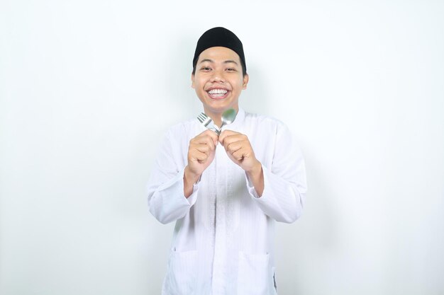 lächelnder muslimischer asiatischer mann mit gekreuztem löffel und gabel wartet auf die pause fasten im ramadan isoliert