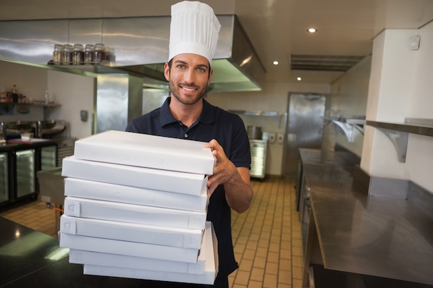 Lächelnder Pizzachef, der Stapel Pizzakästen hält