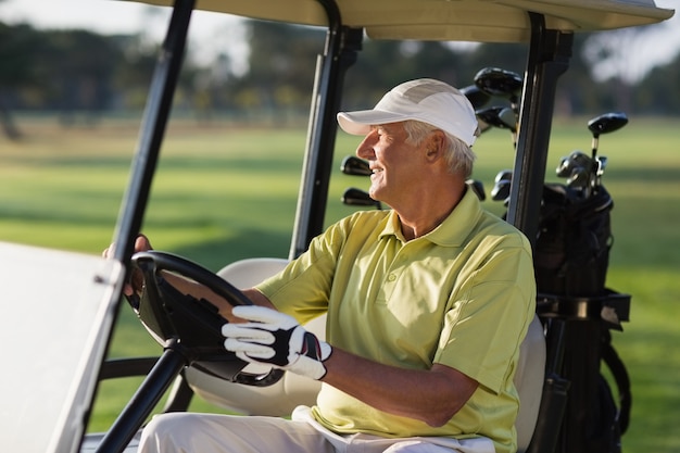 Lächelnder reifer Mann, der Golfbuggy fährt