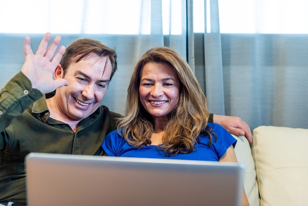 Lächelnder reifer Mann und Frau, die auf Videoanruf mit Laptop sprechen. Foto in hoher Qualität