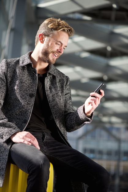 Lächelnder Reisemann, der mit Handy am Flughafen sich entspannt