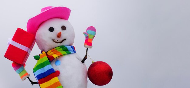 Lächelnder schneemann der weihnachts- und wintermode im hutschal und in den handschuhen mit geschenk- und neujahrsball