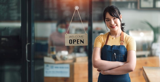 Lächelnder schöner asiatischer Barista, der einladend an einer Cafétür steht