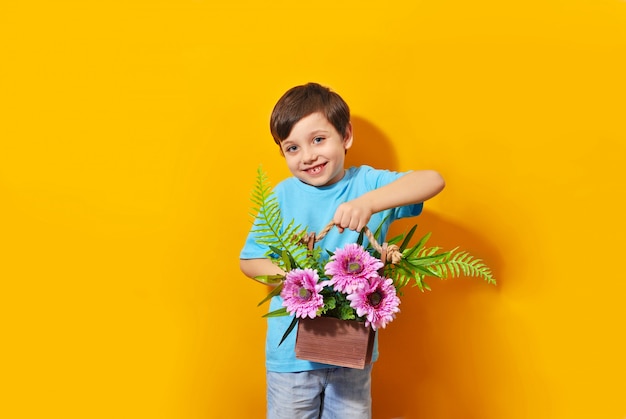 Lächelnder schöner kinderjunge hält blumenstrauß auf dem gelben hintergrund