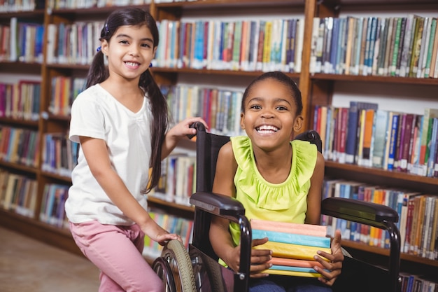 Lächelnder Schüler im Rollstuhl, der Bücher in der Bibliothek hält