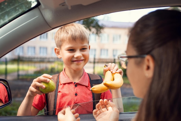 Lächelnder Schuljunge, der Früchte von seiner Mutter nimmt, bevor er zur Schule geht