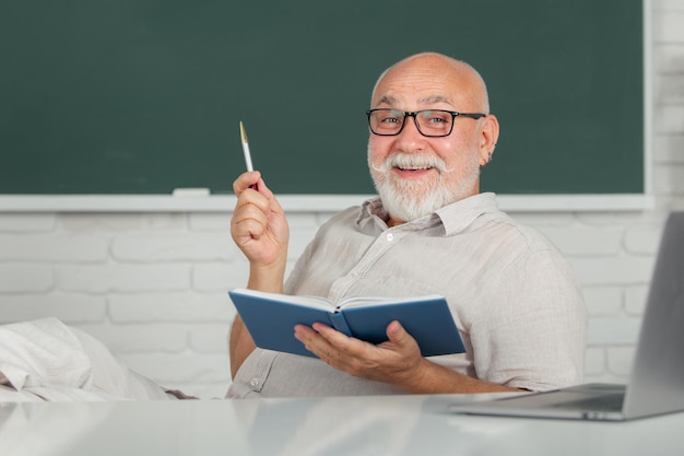 Lächelnder Senior-Lehrer, der im Klassenzimmer an der Tafel unterrichtet Lehrer an der Universität Mann Senior Teac