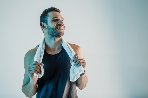 Lächelnder Sportler mit Handtuch. Junger bärtiger europäischer Mann trägt Sportuniform. Auf türkisfarbenem Hintergrund isoliert. Studio-Shooting. Platz kopieren